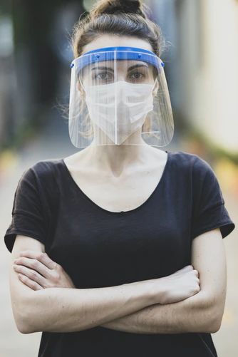 A serious-looking Caucasian brunette female wearing a facemask and face shield