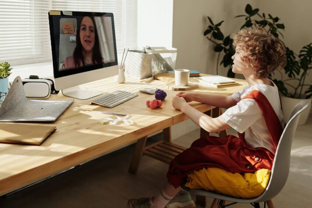A child looking at a laptop as if interacting with a female adult, presumably a teacher, as if on a video call