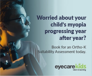 A child wearing spectacles, with a microscope, looking away as if in deep thought in a darkened room.